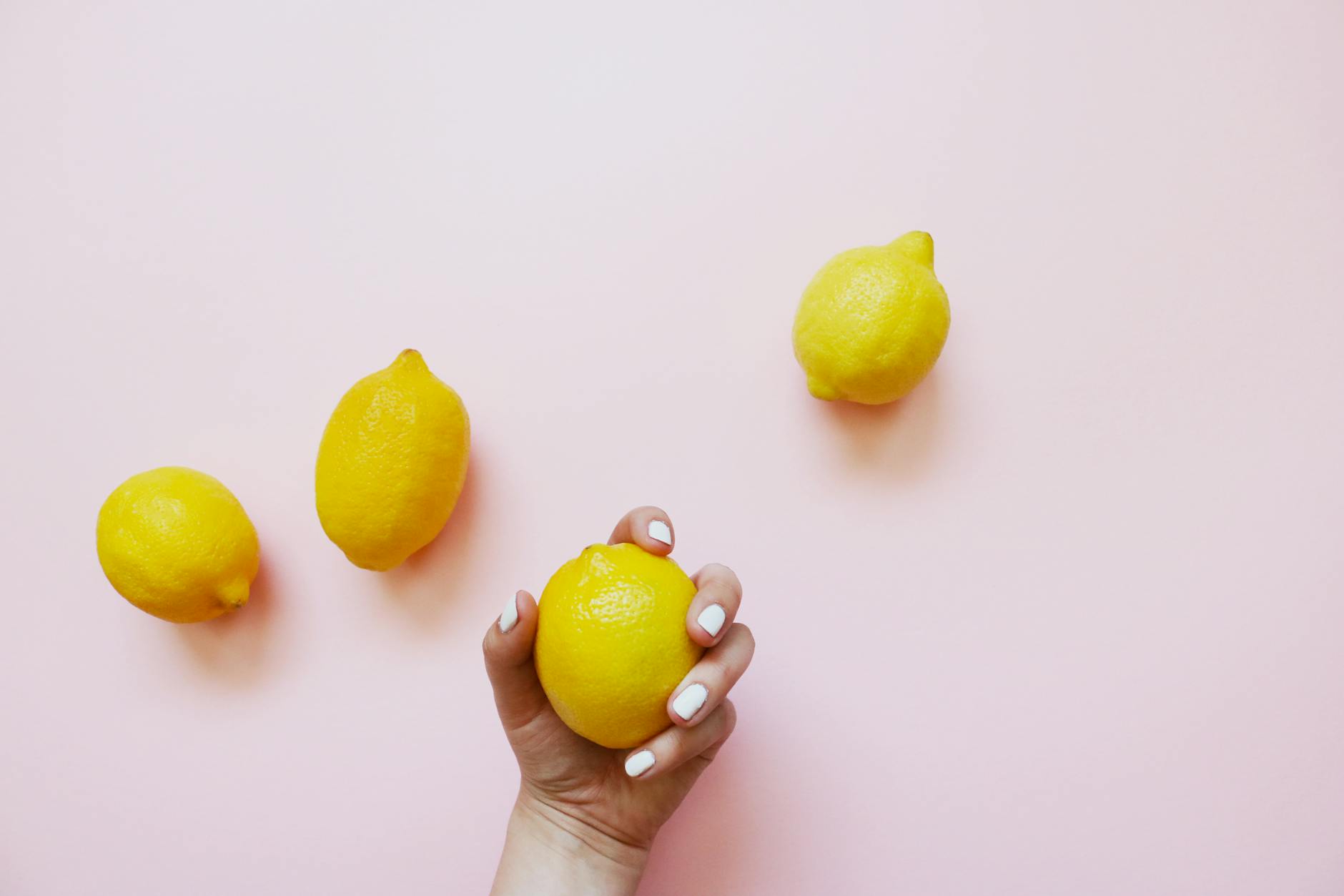 A hand holding a lemon on a soft pink background, symbolizing gentle reconnection with sensation.