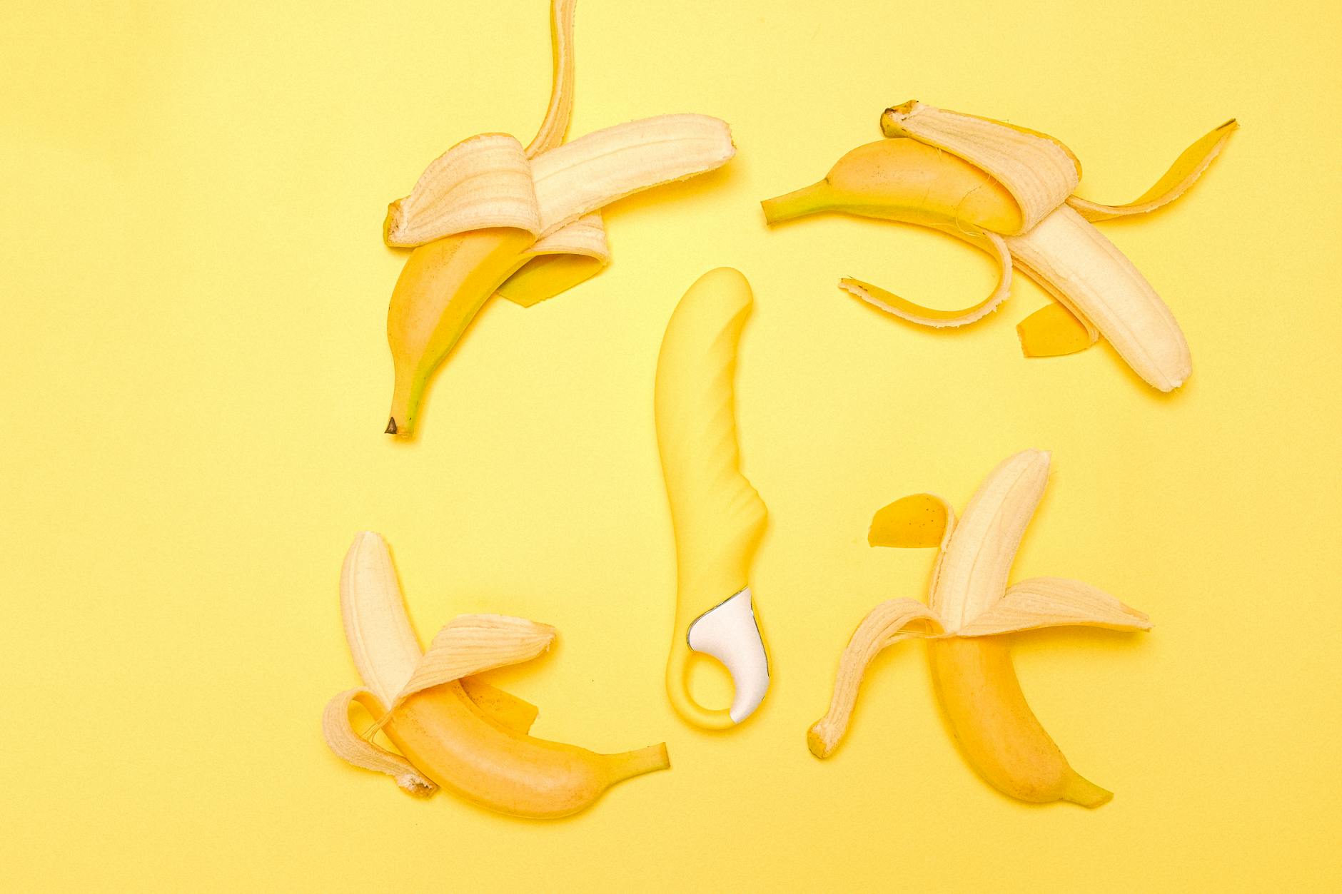 Vibrador de silicona amarilla rodeado de limones pelados sobre fondo amarillo