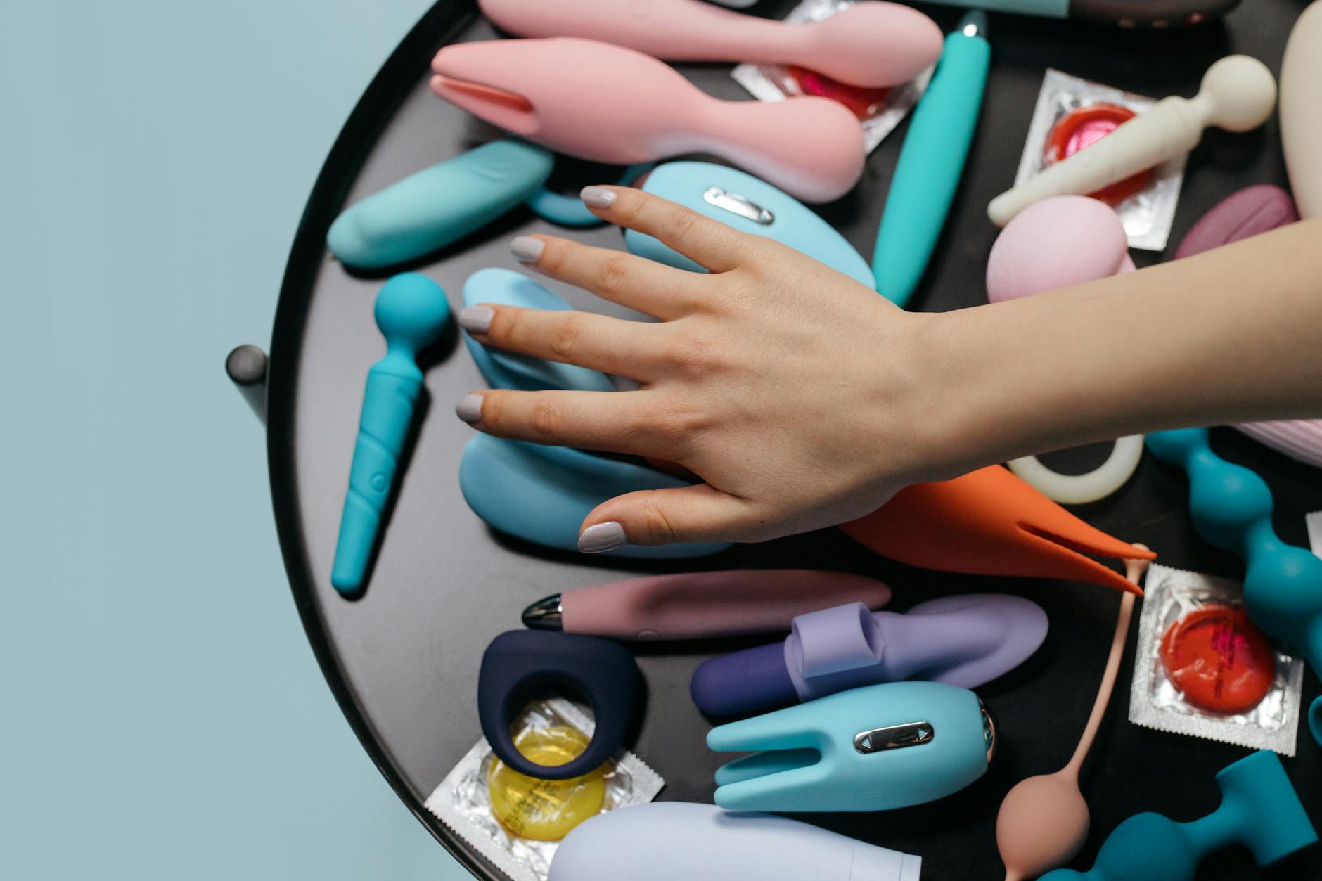 A woman's hands holding a blue clitoral vibrator against a knitted sweater, representing comfort and accessibility