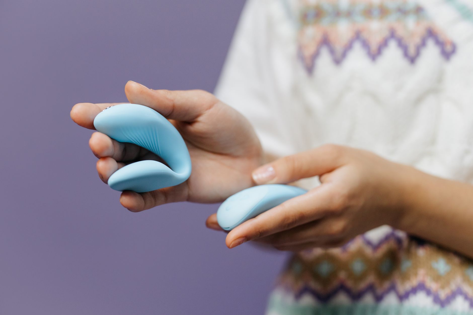 Hand holding a sleek lemon clitoral vibrator against a purple background.