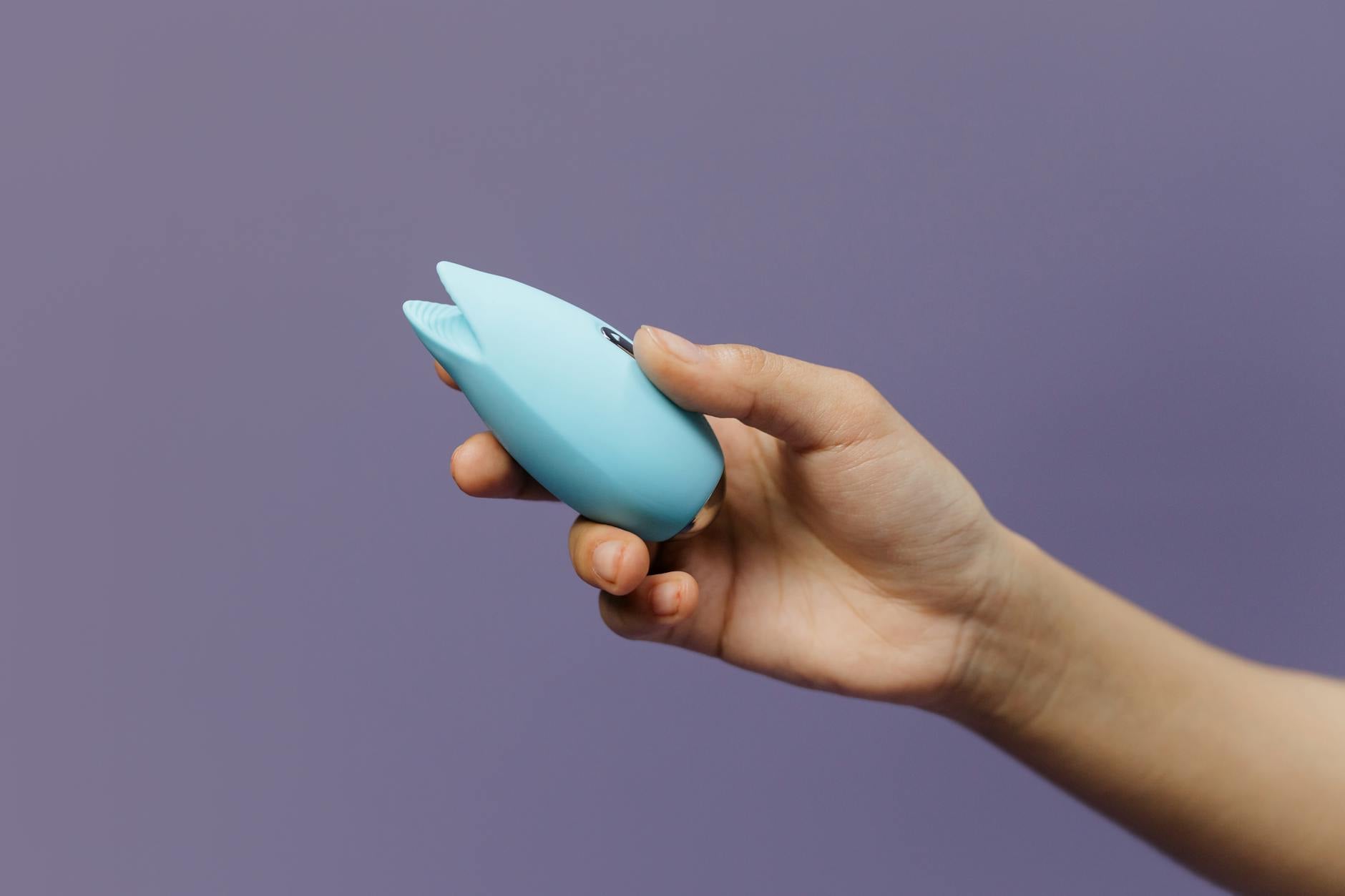 Vibrador de silicona azul sostenido en la mano contra un fondo púrpura sólido, promoviendo el amor propio y la sexualidad