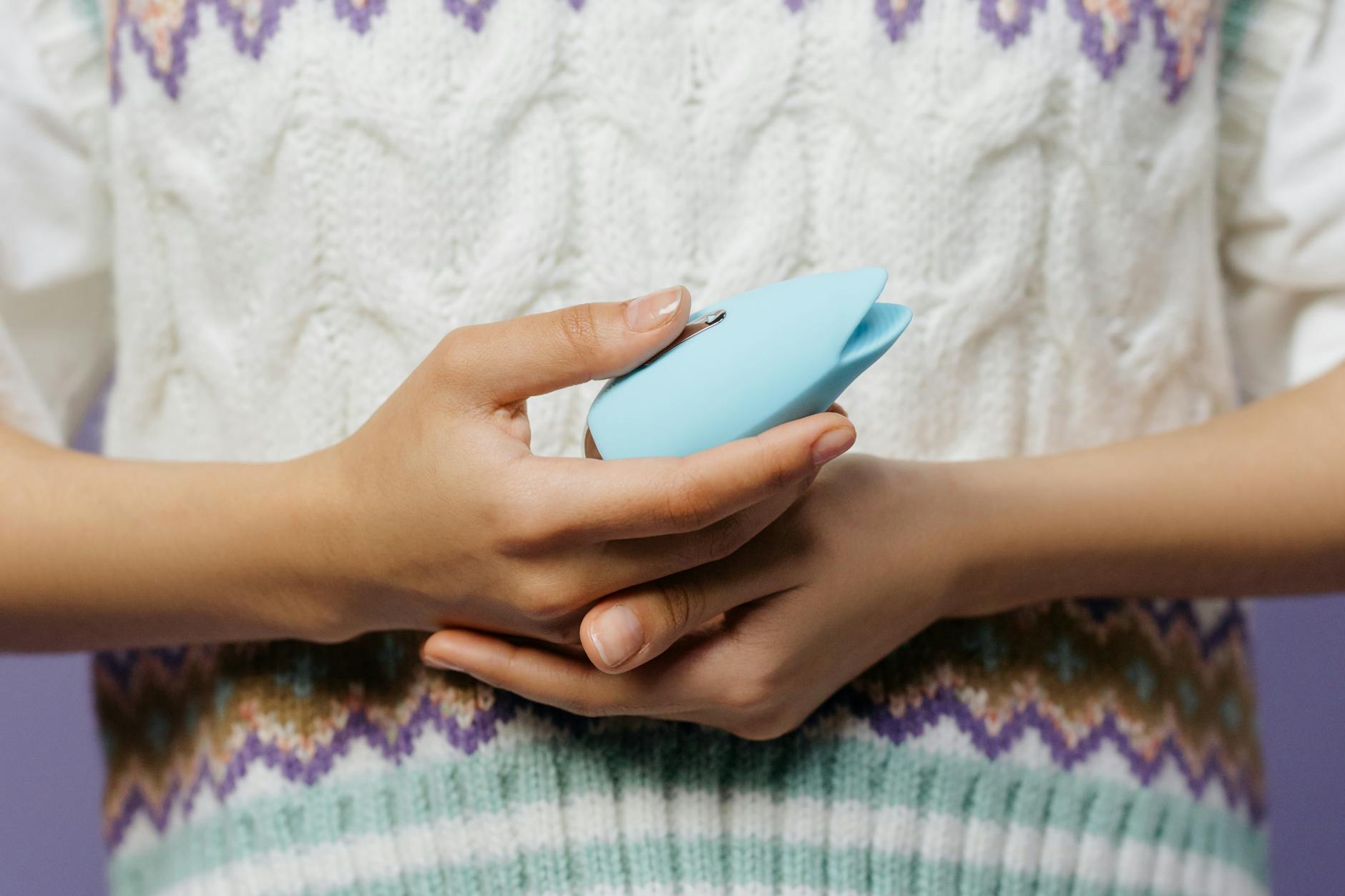 Una mano sosteniendo un juguete sexual de silicona azul contra un fondo morado, promoviendo el amor propio y la sexualidad